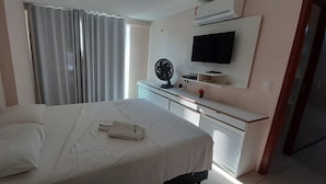 Una habitación de hotel con una cama, un escritorio con un ventilador, un televisor y una ventana con cortinas.
