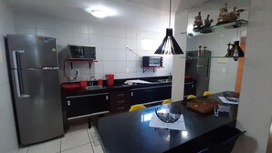 Una cocina moderna con refrigerador, microondas y tostadora. Hay una encimera negra, un lavamanos y una zona de comedor con sillas.