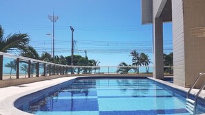 Una piscina con borde de azulejos, rodeada por un muro bajo y una barrera de cristal.