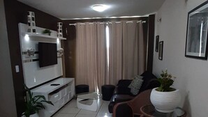 Una sala moderna con mueble de televisión blanco, un sofá y sillas de mimbre.
