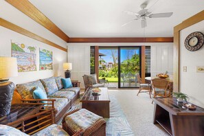 A living room with a sofa, coffee table, and chairs, a dining area with a table and chairs, and a view through glass doors to the outside.