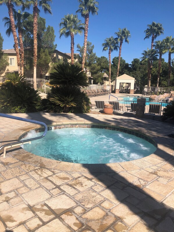 A hot tub surrounded by a pool area with lounge chairs and palm trees.