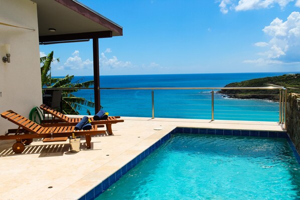 A pool area with lounge chairs and a view of the ocean.