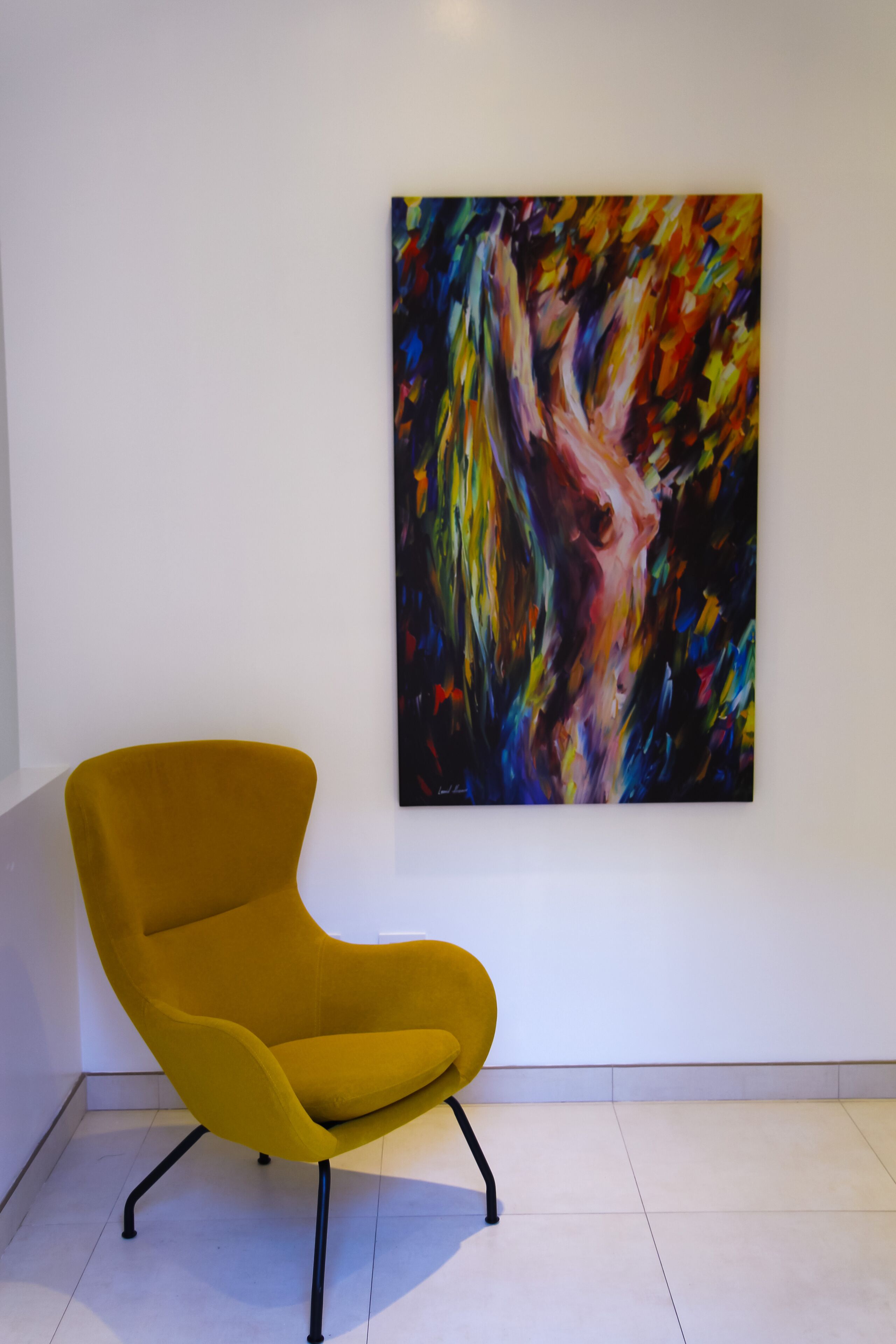 Uma cadeira amarela moderna numa sala com um quadro abstrato e colorido na parede.