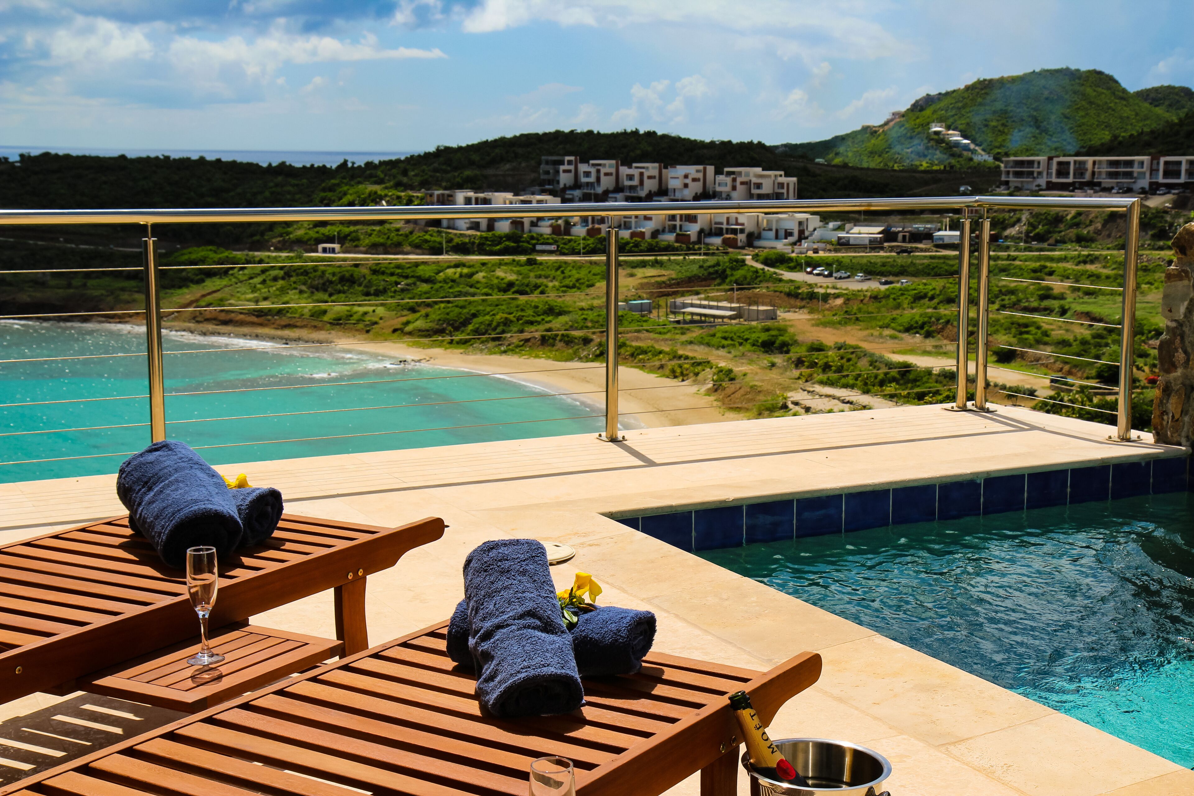 Uma área à beira da piscina com espreguiçadeiras de madeira, uma taça de champanhe e uma garrafa de champanhe.
