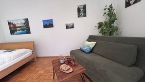 A modern, minimalist room with a wooden floor, a bed, a green sofa, and a small wooden table with bread and mugs. - Fewo Ideale Lage Wohn/Schlafzimmer Bad /WC Terrasse (Bad Reichenhall)