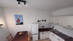A compact kitchen with white cabinets, a wooden dining table, and a refrigerator. - Fewo Ideale Lage Wohn/Schlafzimmer Bad /WC Terrasse (Bad Reichenhall)