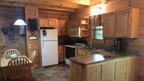 Una cocina tipo cabaña de madera con una isla central, armarios de madera, un refrigerador, un microondas y un fregadero.