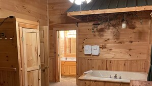 Un dormitorio de cabaña de madera con una cama, un ventilador de techo, un baño con bañera y una puerta de madera.