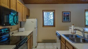 Une cuisine avec des meubles en bois, un poêle noir, un réfrigérateur blanc et une fenêtre donnant sur les arbres.