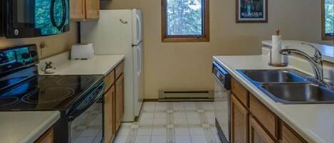 A kitchen with wooden cabinets, a black stove, a white refrigerator, and a window with a view of trees.