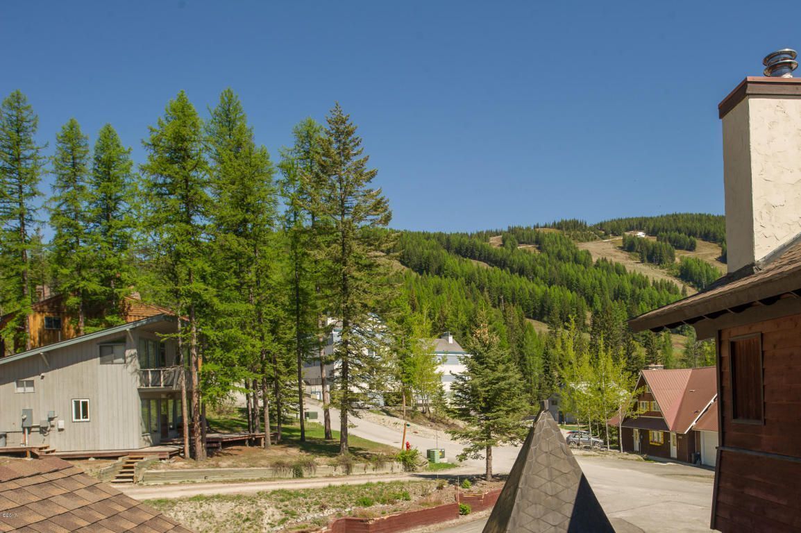 A residential area with houses, a clear sky, and a forested hillside in the background.
