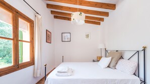 A bedroom with a bed, a window with curtains, a hanging light fixture, and a bedside table with a lamp. - Villa with pool and view – Finca Can Guixe (Sóller)