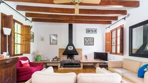 A living room with a fireplace, wooden beams, a red chair, a beige sofa, and a television. - Villa with pool and view – Finca Can Guixe (Sóller)