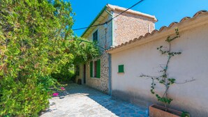 A narrow cobblestone alleyway with a stone building, a potted plant, and a clear blue sky. - Villa with pool and view – Finca Can Guixe (Sóller)