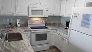 Una cocina con armarios blancos, microondas, horno, lavamanos y refrigerador.