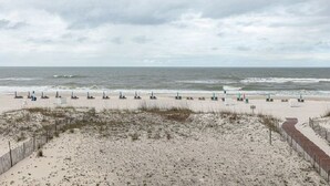 Una playa con hileras de sillas y sombrillas, un camino de arena y una valla de madera.