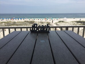 A wooden deck with a metal sign spelling "Beach" and a view of the beach with umbrellas and people.