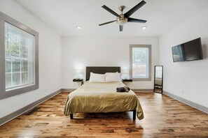 Ein Schlafzimmer mit einem Bett, einem Deckenventilator, einem Fernseher und einem Fenster.