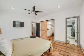 A bedroom with a bed, a ceiling fan, a TV, and a wooden door leading to a bathroom.