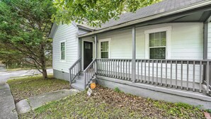 A two-story house with a front porch, a small front yard, and a tree.