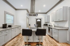 A modern kitchen with granite countertops, stainless steel appliances, and a central island with two black bar stools.