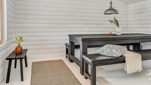 Ein Zimmer mit einem dunklen Holztisch und einer Bank, einer hängenden Pendelleuchte, einem kleinen Topfpflanzen und einem gewebten Teppich.