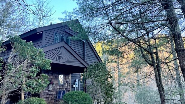Eine rustikale Holzhütte mit geneigtem Dach, umgeben von Bäumen und einer Schotterauffahrt.