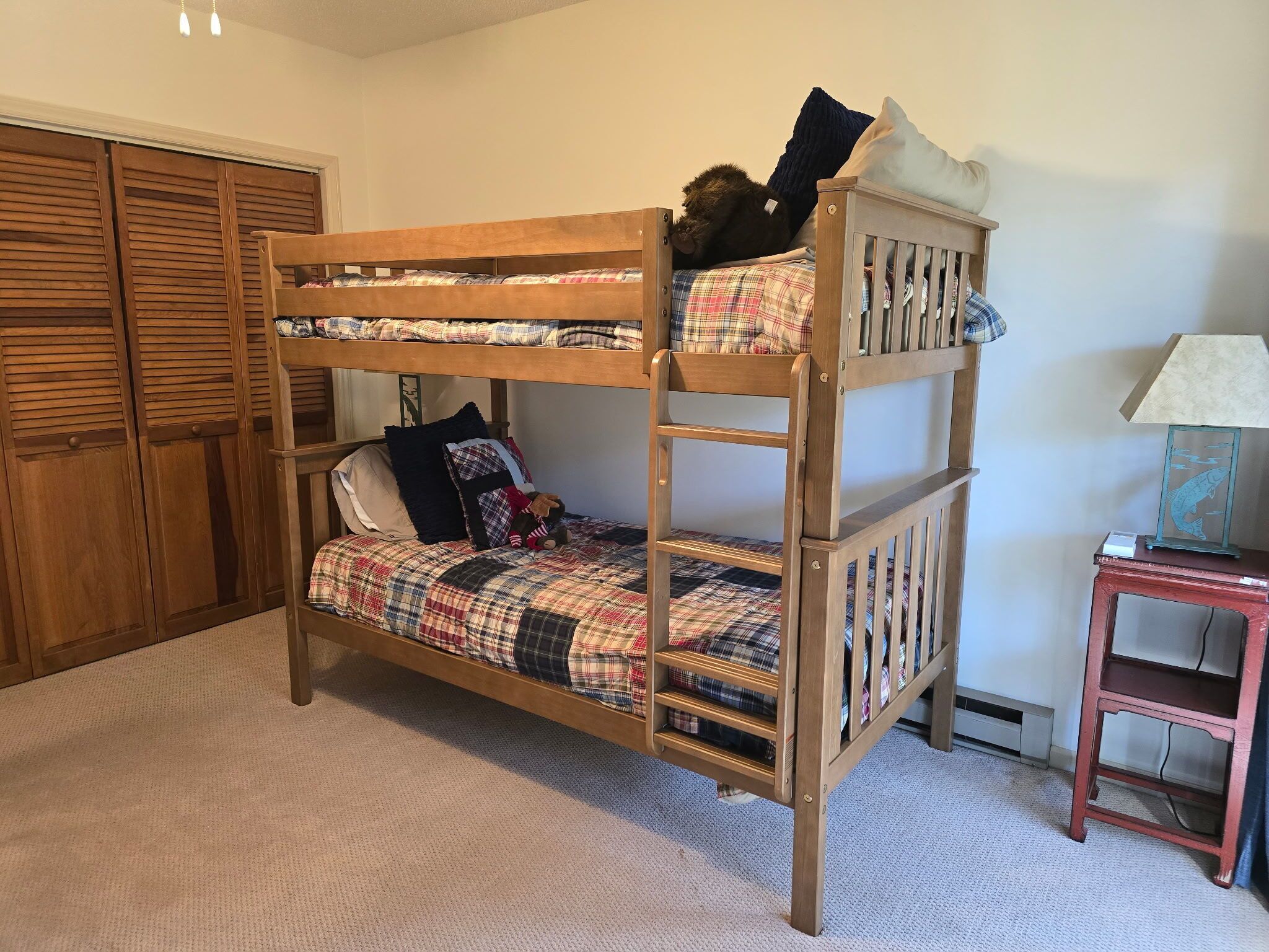 A bunk bed with plaid bedding, a wooden headboard, and a small bedside table with a lamp.