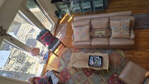 Ein gemütliches Wohnzimmer mit einer braunen Ledersofa, gemusterten Kissen, einem gewebten Couchtisch und einem farbenfrohen Teppich.
