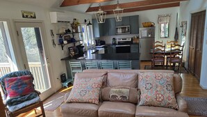 Ein gemütliches Wohnzimmer mit einem braunen Ledersofa, einem Essbereich mit Holzsesseln und einer Küche mit blauen Schränken und einer schwarzen Arbeitsplatte.