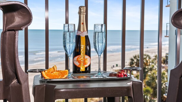 Un tavolo con una bottiglia di champagne Chandon, due bicchieri e un piatto di frutta su un balcone con vista sulla spiaggia.