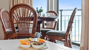 Zona pranzo con sedie in legno e tavolo apparecchiato per un pasto, con vista su un balcone e sull'oceano.
