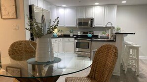 Een moderne keuken met witte kastjes, roestvrijstalen apparatuur en een glazen eettafel met rieten stoelen.