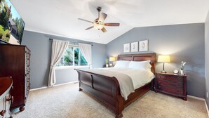 A bedroom with a large bed, a ceiling fan, a window with curtains, a dresser, and a nightstand with a lamp and clock. - Hot Tub, Luxury King Bed & Yard Games ~ Quiet & Serene w Incredible Yard (Erie)