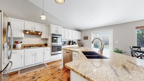 A modern kitchen with white cabinets, stainless steel appliances, granite countertops, and a large island with a sink. - Hot Tub, Luxury King Bed & Yard Games ~ Quiet & Serene w Incredible Yard (Erie)