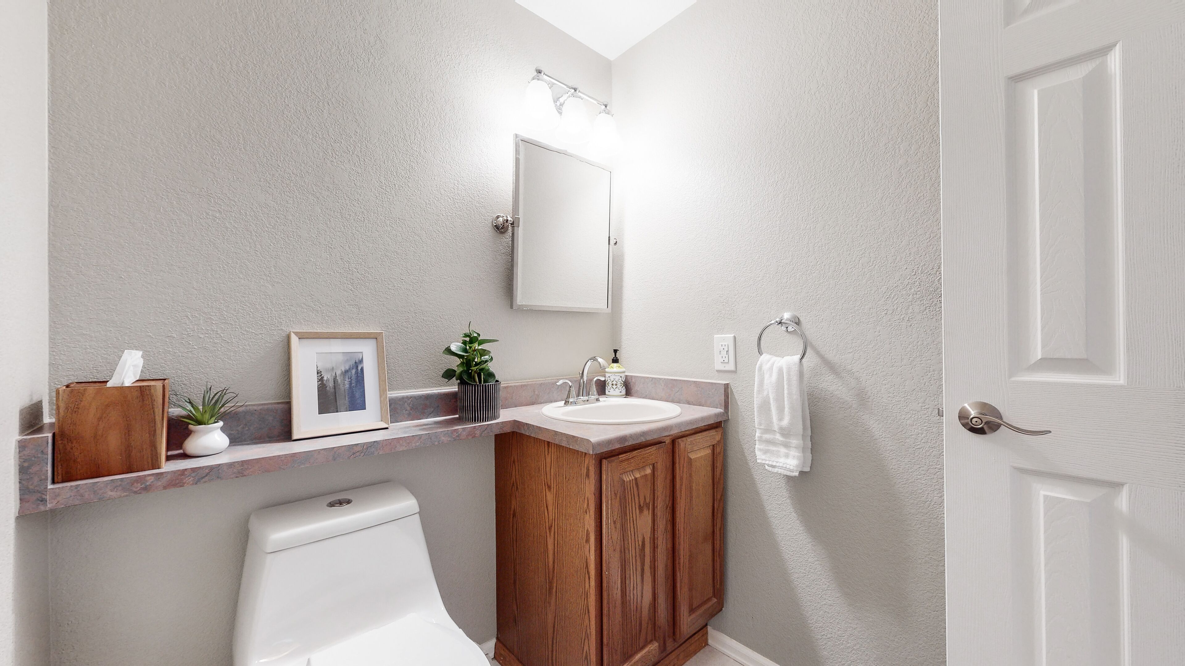 Une salle de bain avec un meuble-lavabo en bois, un lavabo blanc, un tableau encadré, une plante en pot et un porte-serviettes.