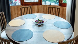 Een ronde tafel met zes stoelen, een schaal fruit en een uitzicht op een boom en gebouwen door grote ramen.