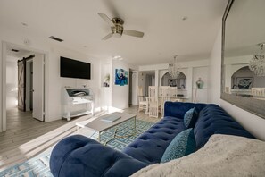 A modern living room with a blue sofa, a white coffee table, and a ceiling fan.