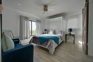 A bedroom with a large bed, a chair, a table, and a window with curtains. - Chic Waterfront Condo in Cape Canaveral - 5 min from the beach! (Cape Canaveral)