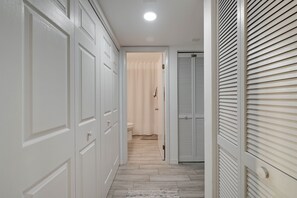 A hallway with white doors, a bathroom visible through an open door, and a window with blinds. - Chic Waterfront Condo in Cape Canaveral - 5 min from the beach! (Cape Canaveral)