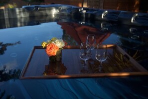 Una mesa de cristal con un jarrón de flores y dos copas de vino vacías sobre una superficie reflectante.