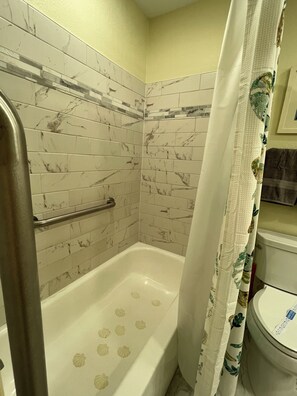 Ein Badezimmer mit einer weißen Badewanne, einer Duschvorhang und einer Haltestange.