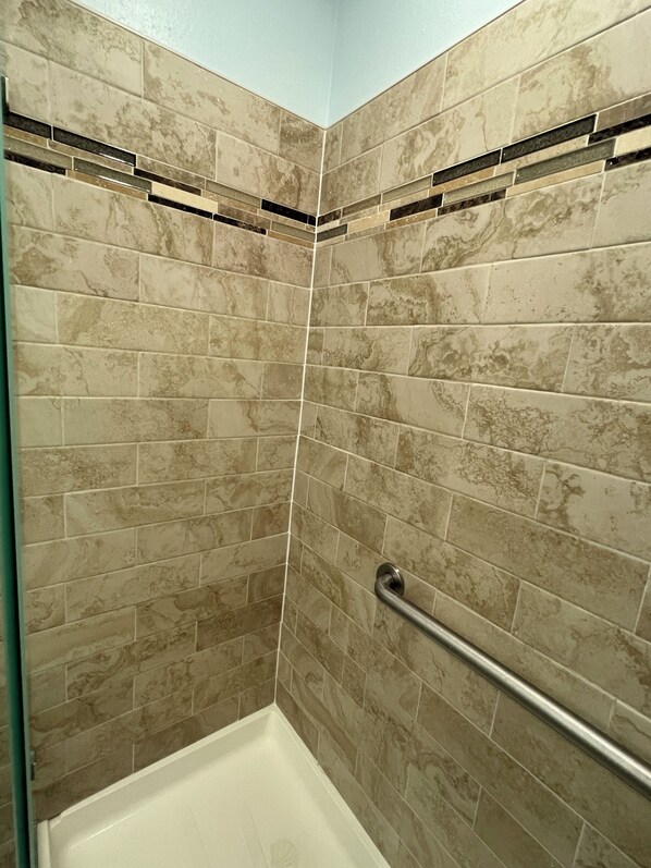 Zona de ducha con azulejos color beige y una barra de apoyo de metal.
