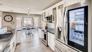 A modern kitchen with white cabinetry, stainless steel appliances, a refrigerator with a freezer, and a dining area with a table and chairs. - Top Choice for Guests, Golf, HPool~Spa, Bachelorettes, Quick Walk for Groceries (Scottsdale)