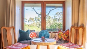 A cozy seating area with two wooden chairs, a round wooden table, and a window with curtains. - Wooshwood: Enchanting rural getaway, pet friendly (Shadforth)