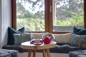 Un rincón acogedor con una mesa redonda de madera, un hervidor de té y una taza, frente a una ventana que ofrece vistas al verdor.