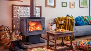 A cozy living room with a wood-burning stove, a sofa, a coffee table with a plate of food and wine glasses, and a colorful rug. - Wooshwood: Enchanting rural getaway, pet friendly (Shadforth)
