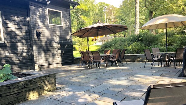 Une terrasse extérieure avec un sol en pierre, des chaises en métal et des parasols.