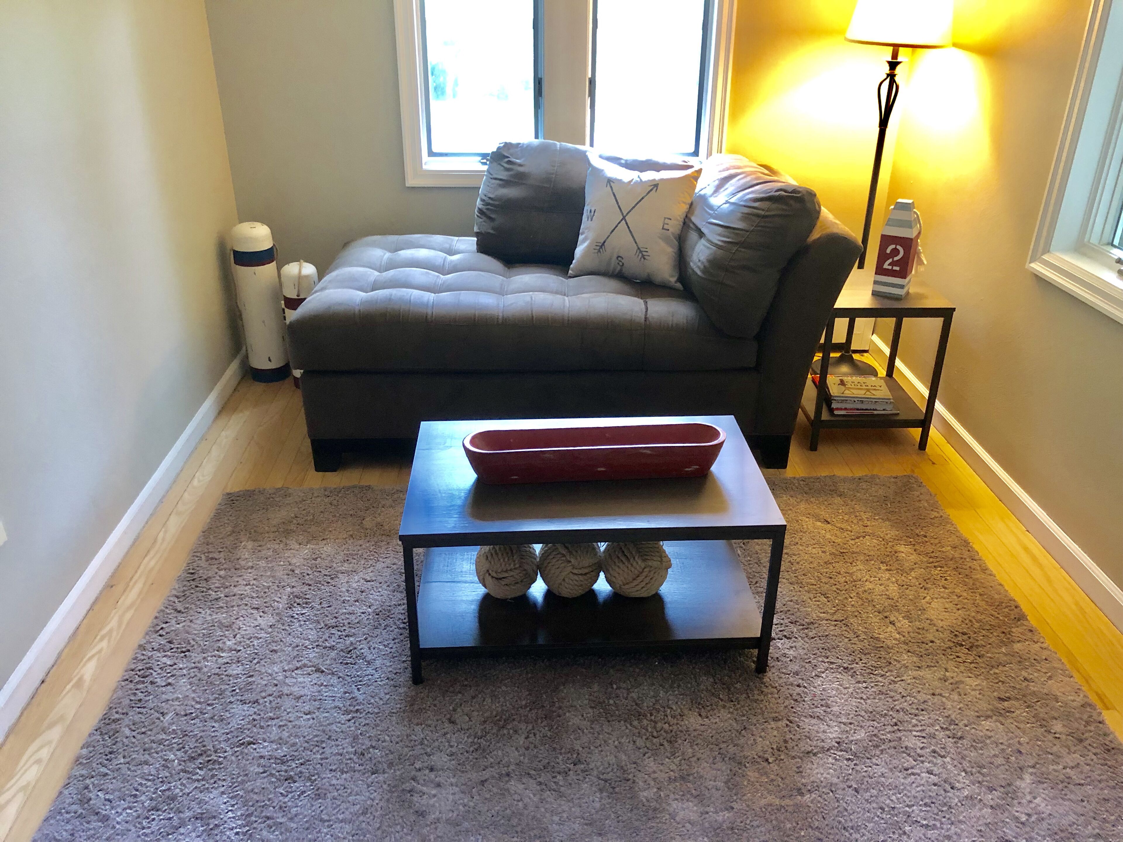 Ein Wohnzimmer mit grauem Sofa, einem kleinen Tisch mit roter Ablage und einer Lampe.